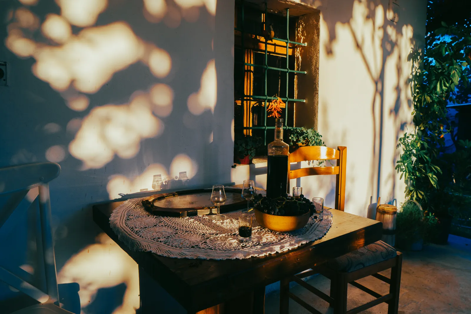 A dinner table set outside an Albanian house at golden hour, with a bottle of wine and glasses