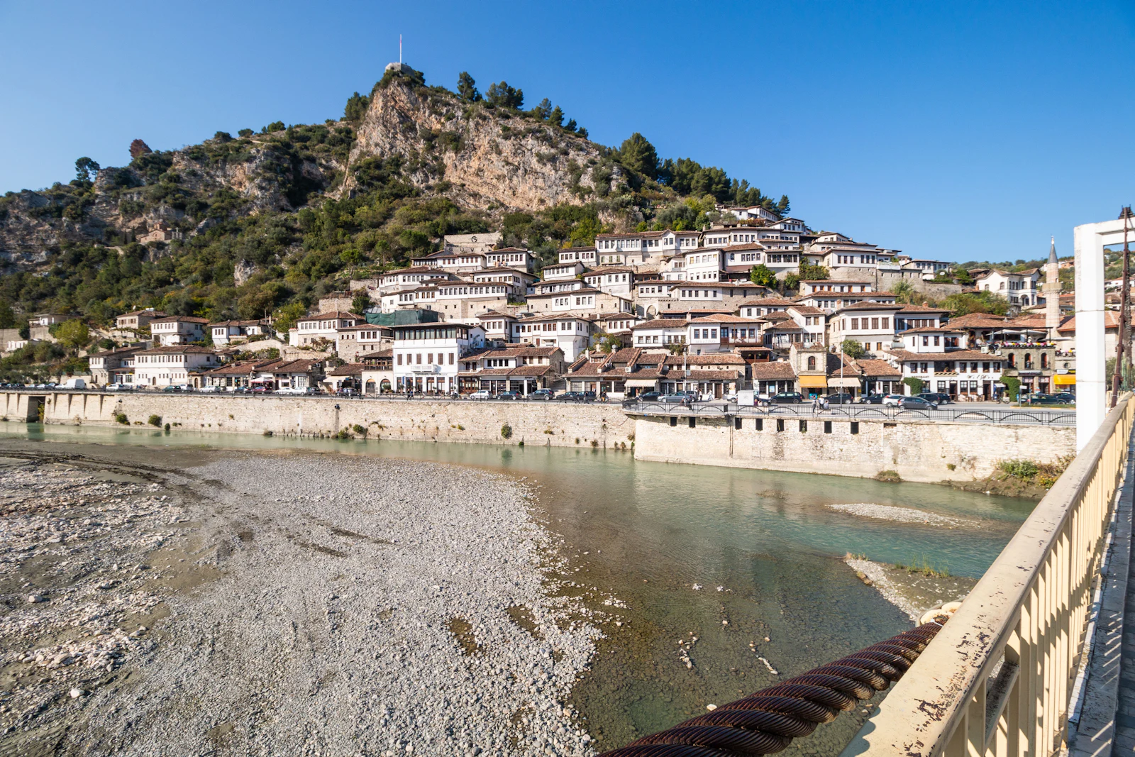 The Osum River running past the Mangalem riverfront in Berat, with the castle hill above