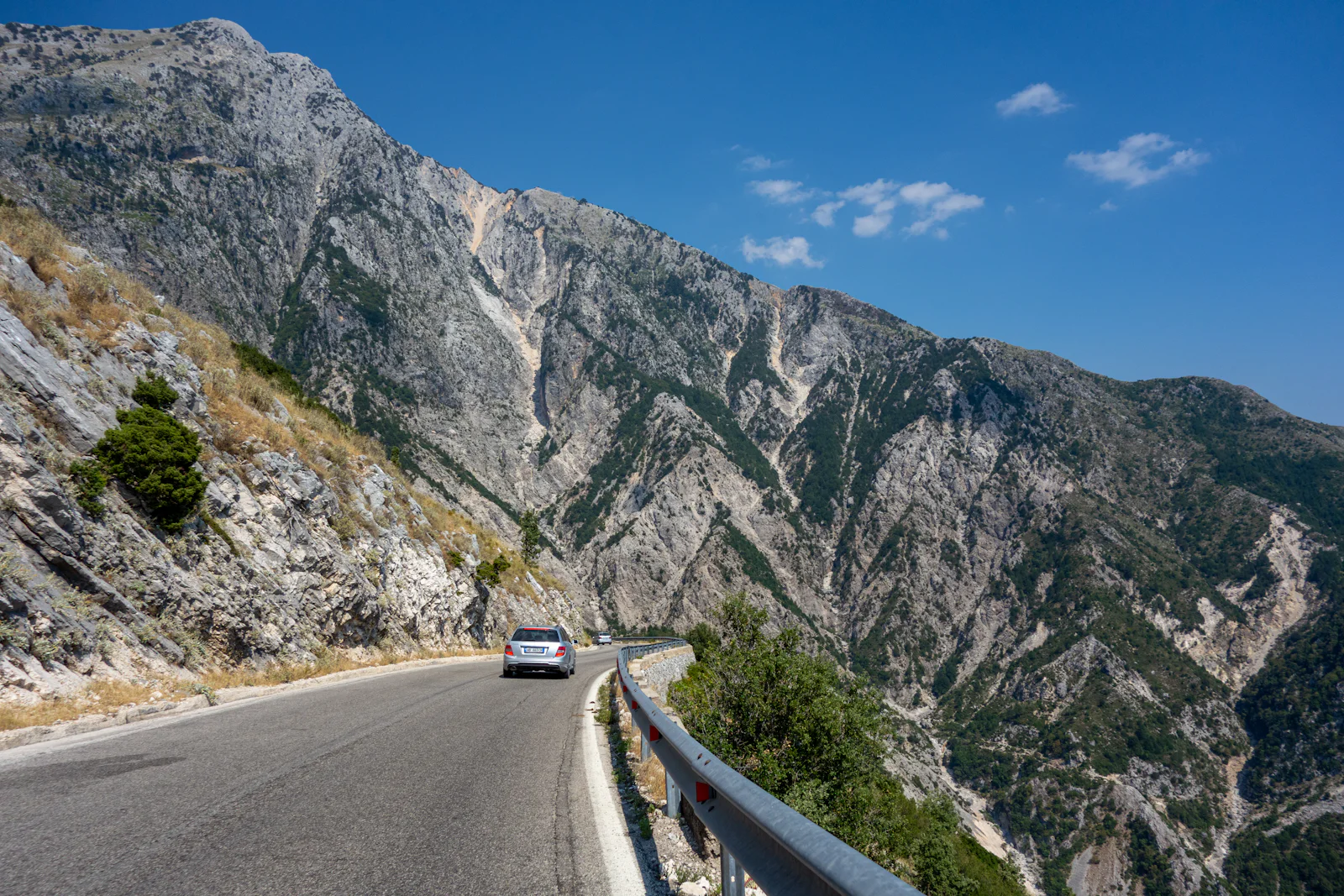 A car on the SH8 road climbing over the Llogara Pass between bare mountains