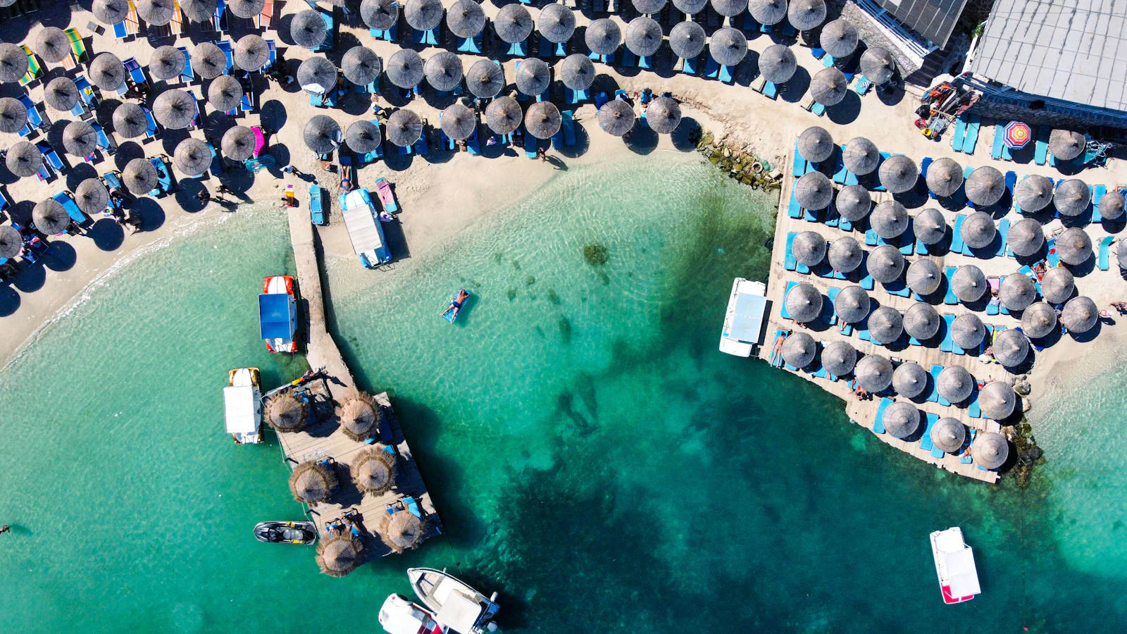 Ksamil beach from above: rows of straw umbrellas, a small jetty and clear turquoise water