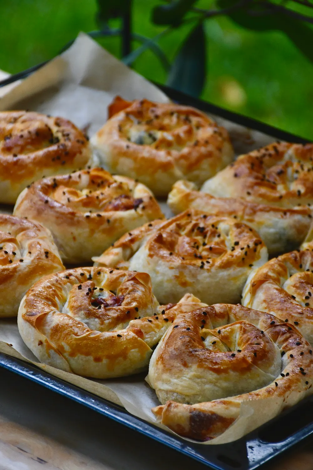 A tray of freshly baked spiral byrek pastries sprinkled with nigella seeds