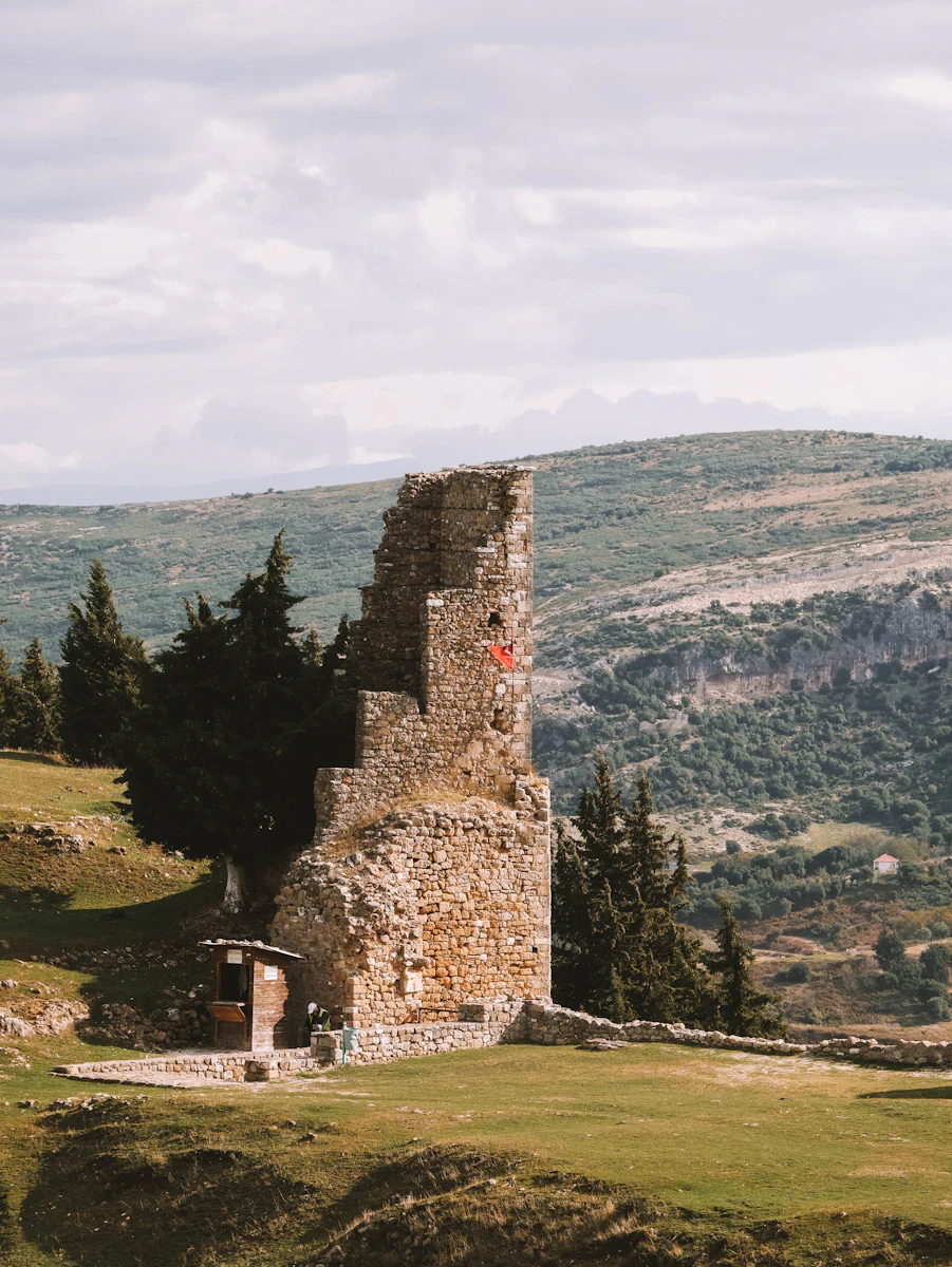 Ruined stone tower of Kaninë Castle with an Albanian flag, on the hill above Vlorë
